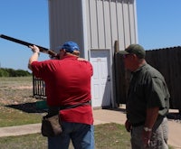 two men standing next to each other shooting a shotgun